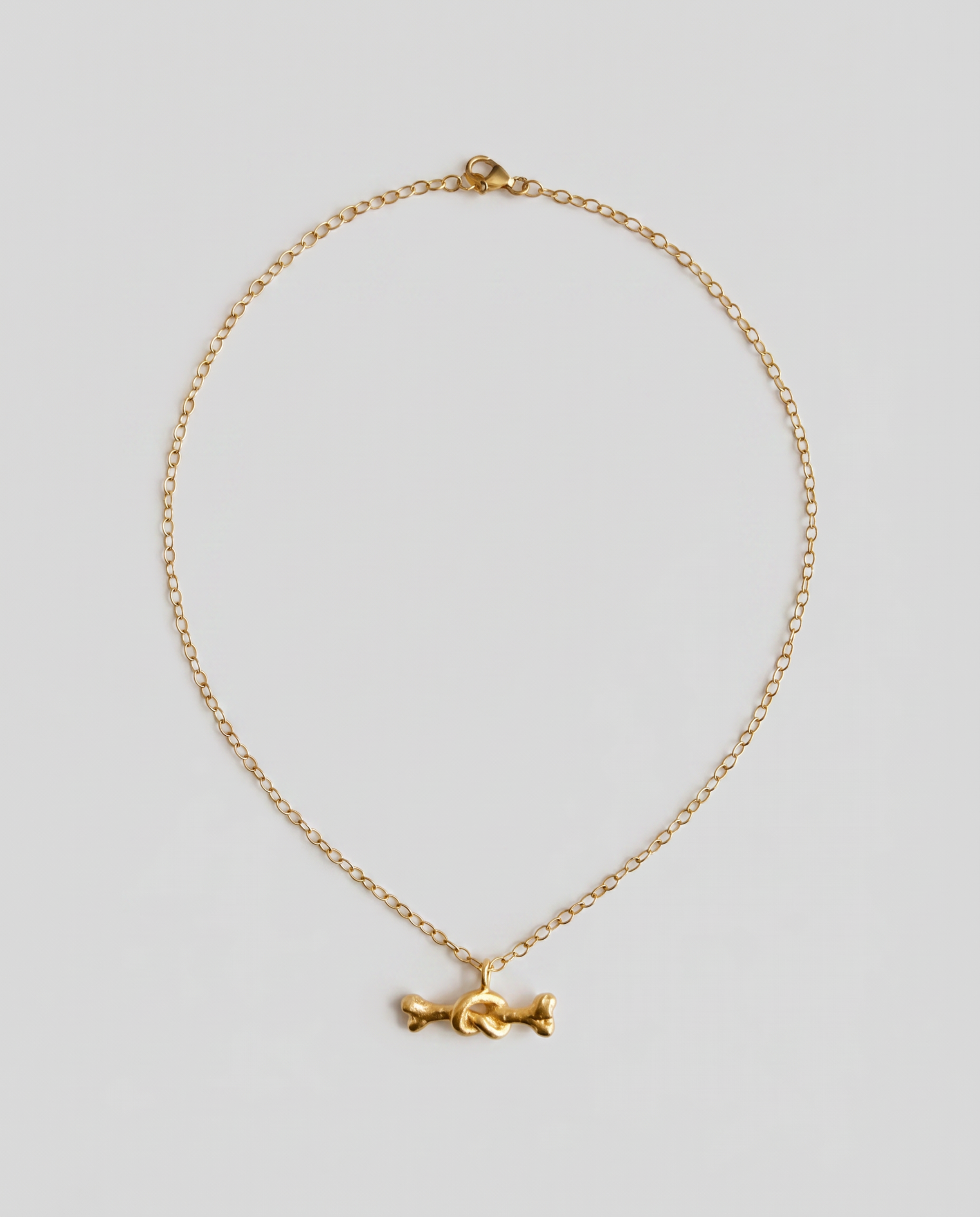 A delicate gold chain necklace featuring a small, stylized gold bone charm in the center, displayed against a solid light gray background.