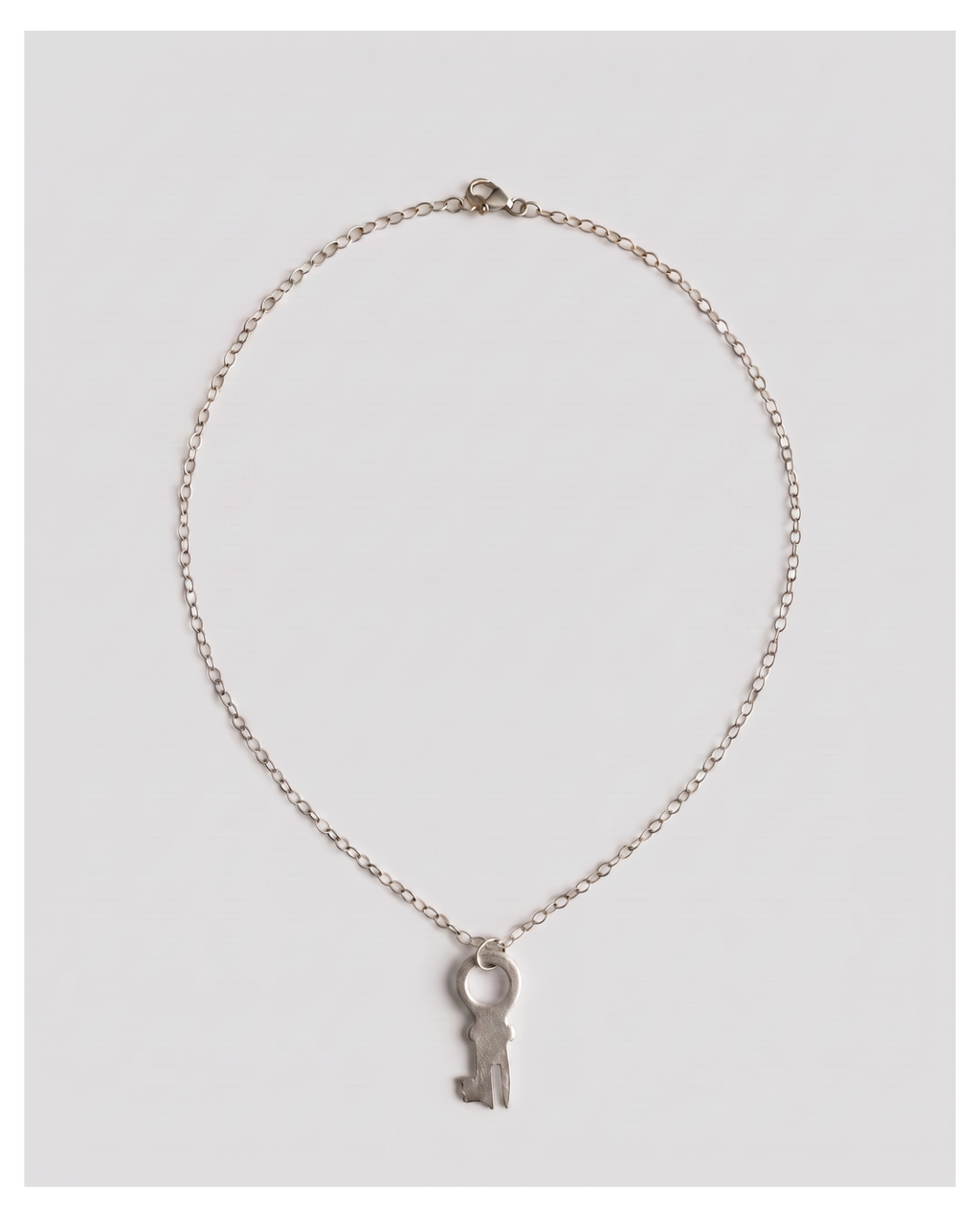 A delicate silver chain necklace featuring a small key-shaped pendant, displayed against a light gray background.