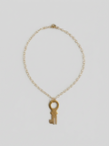 A delicate gold chain necklace featuring a vintage-style skeleton key pendant, displayed against a neutral light gray background.