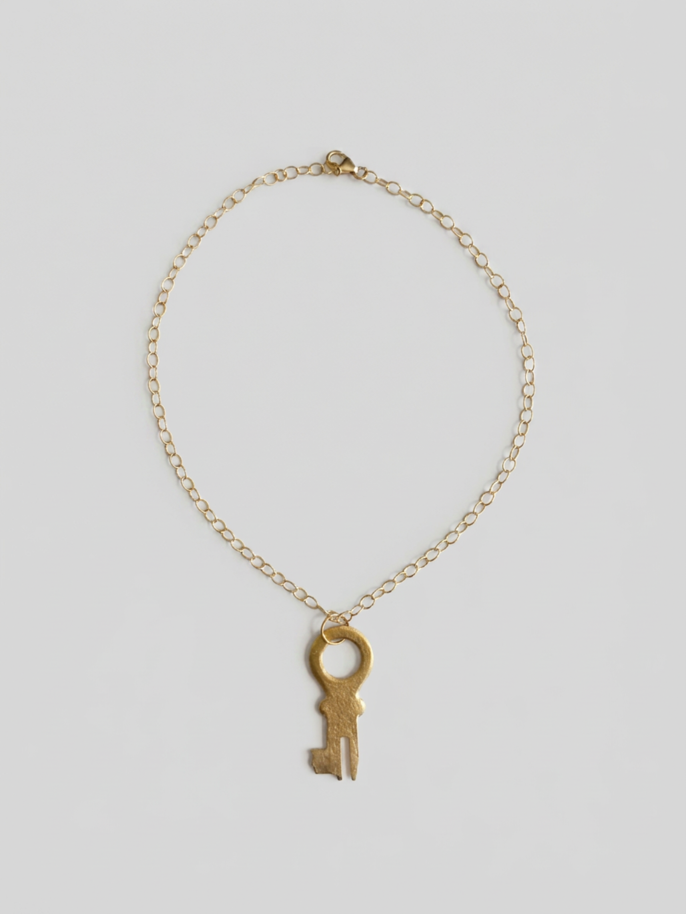 A delicate gold chain necklace featuring a vintage-style skeleton key pendant, displayed against a neutral light gray background.