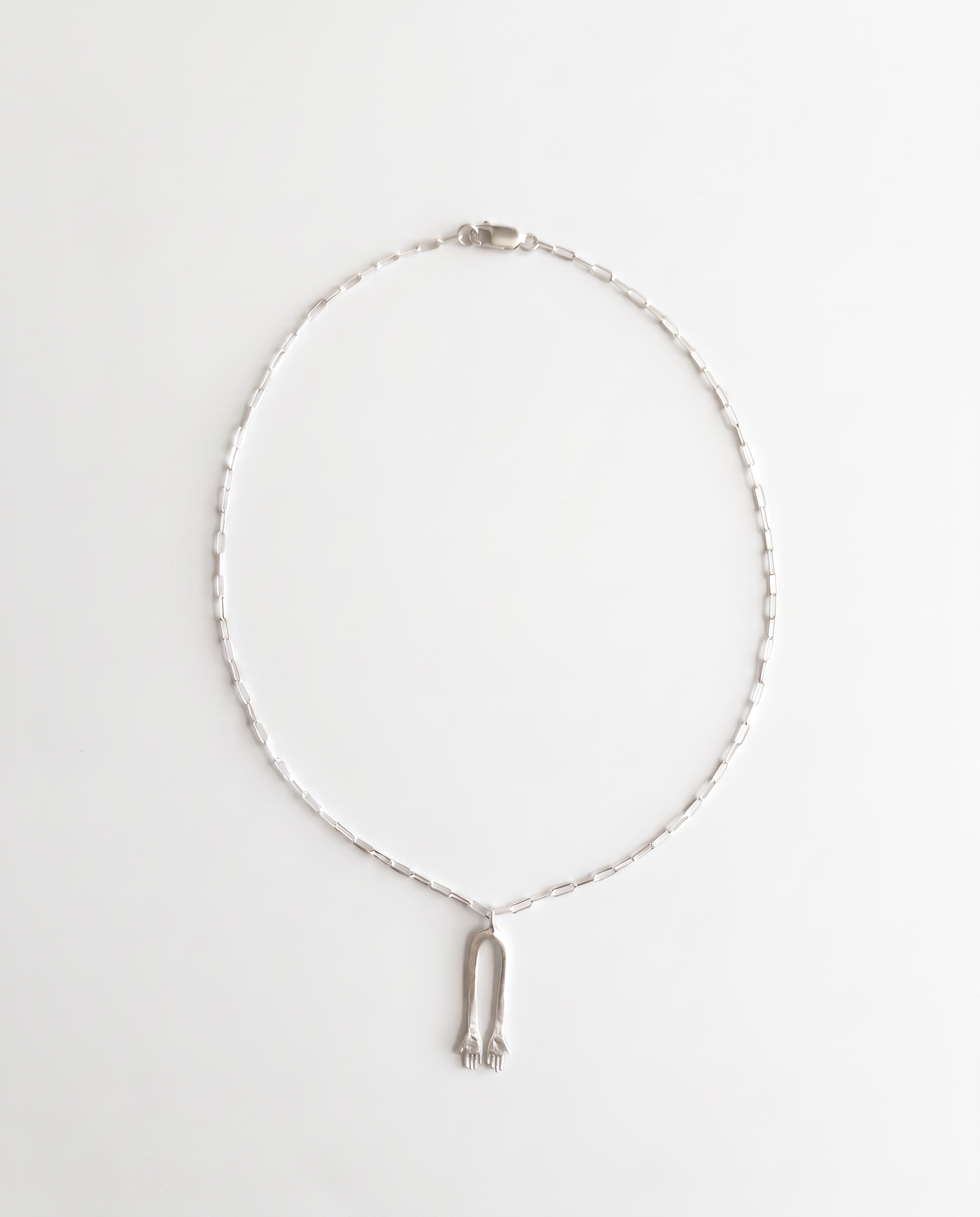 A silver chain necklace with a small silver pendant shaped like a stylized hamsa, displayed on a clean white background.