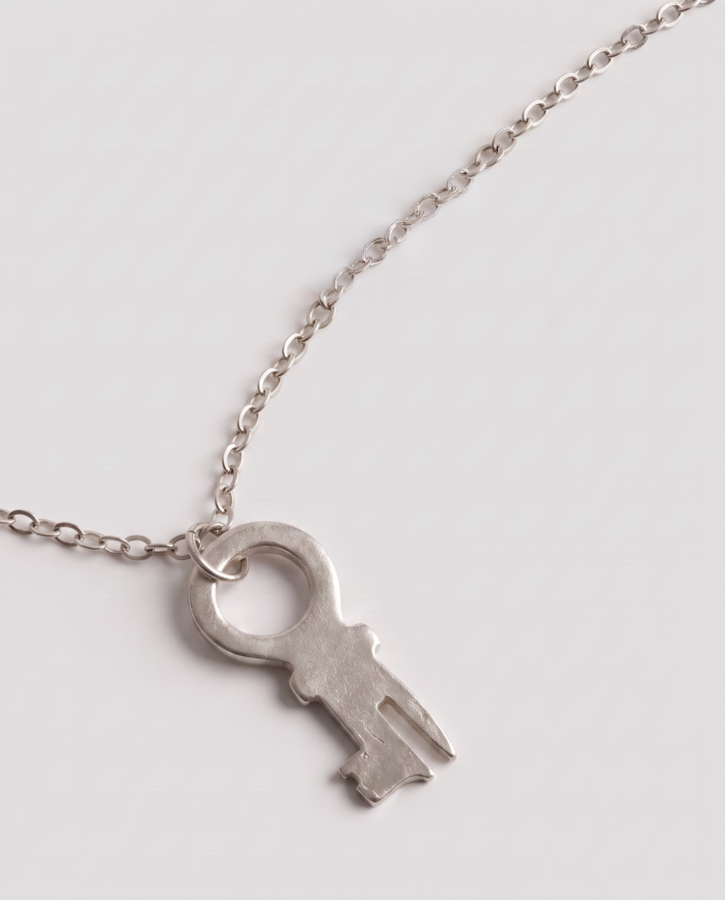 A silver key-shaped pendant necklace on a delicate silver chain, photographed on a clean light gray background.